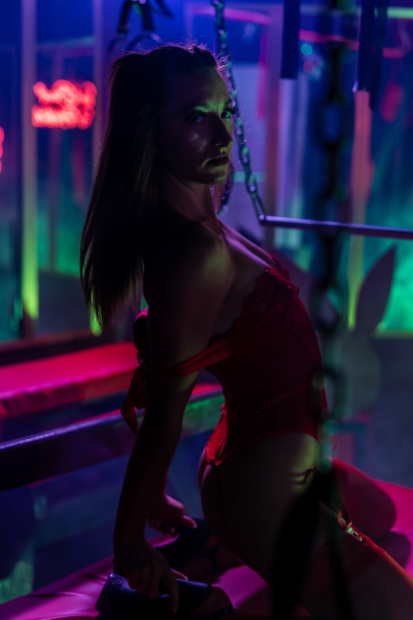 Sensual portrait of woman in red lingerie with neon glow lighting in an after-dark boudoir set.