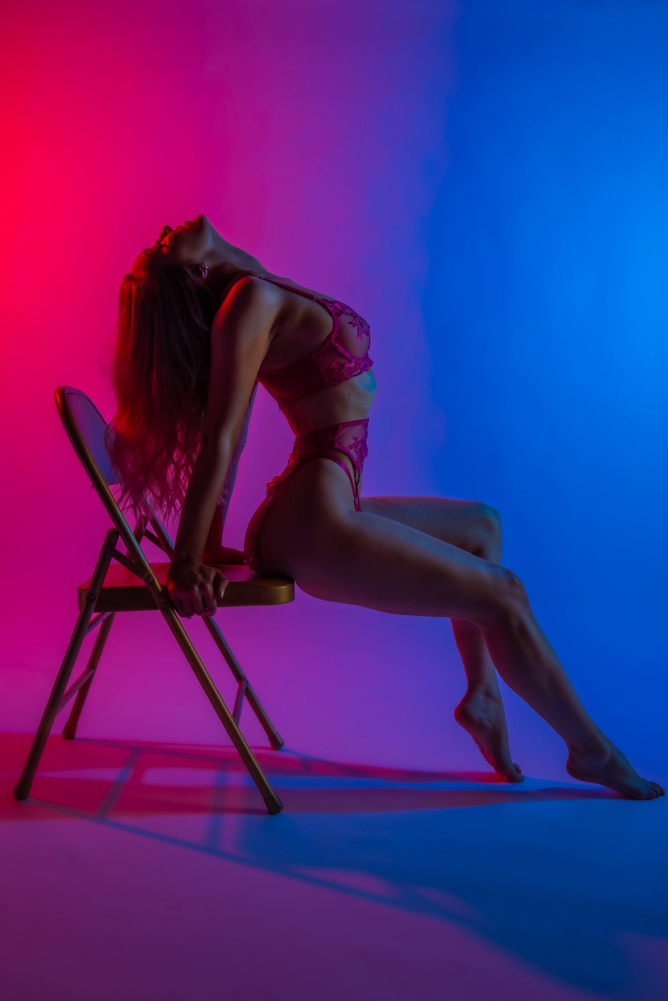 Boudoir model leaning over a chair with deep blue lighting.