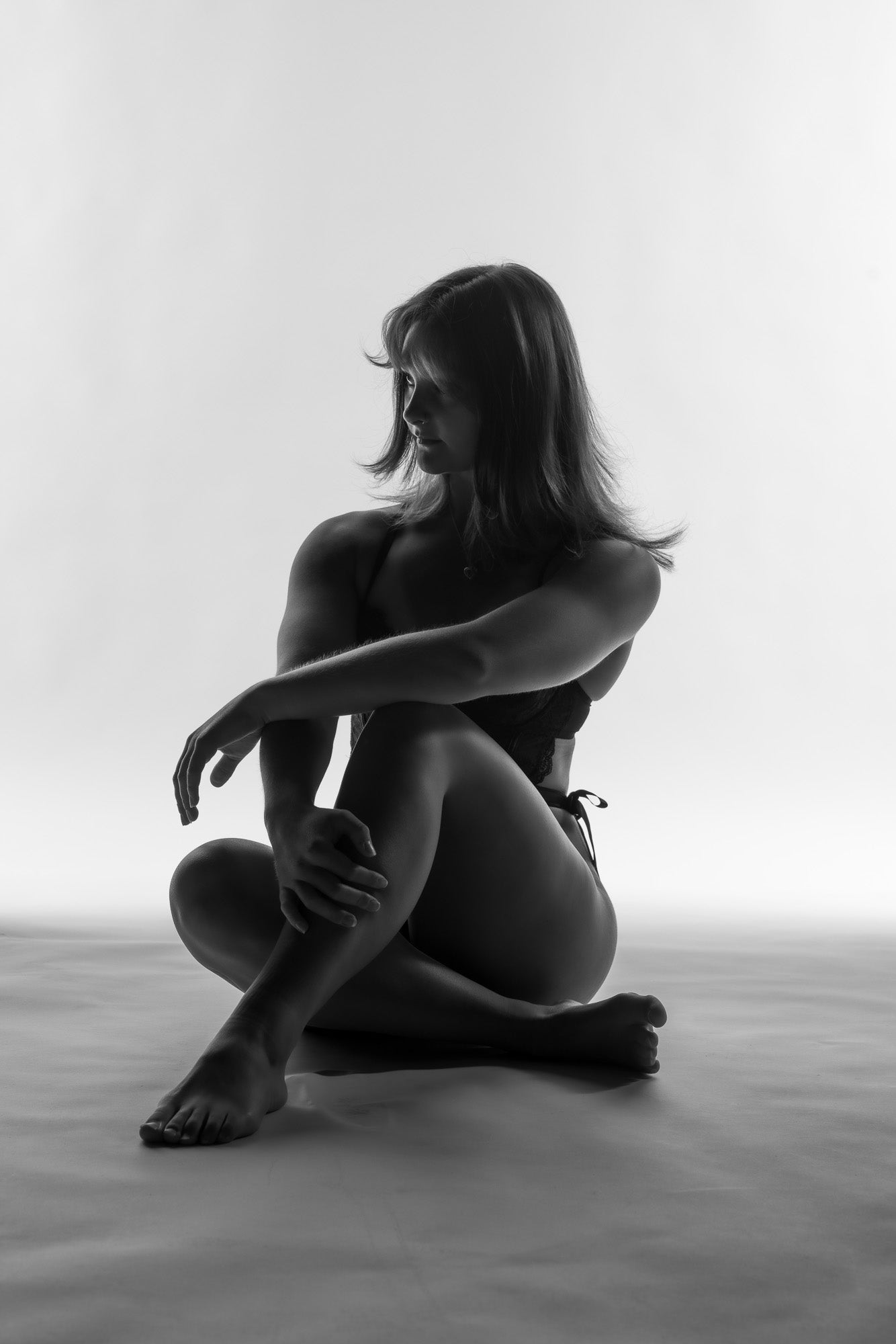 Black and white boudoir silhouette portrait featuring a seated pose with dramatic backlighting, creating a timeless, artistic, and intimate aesthetic.