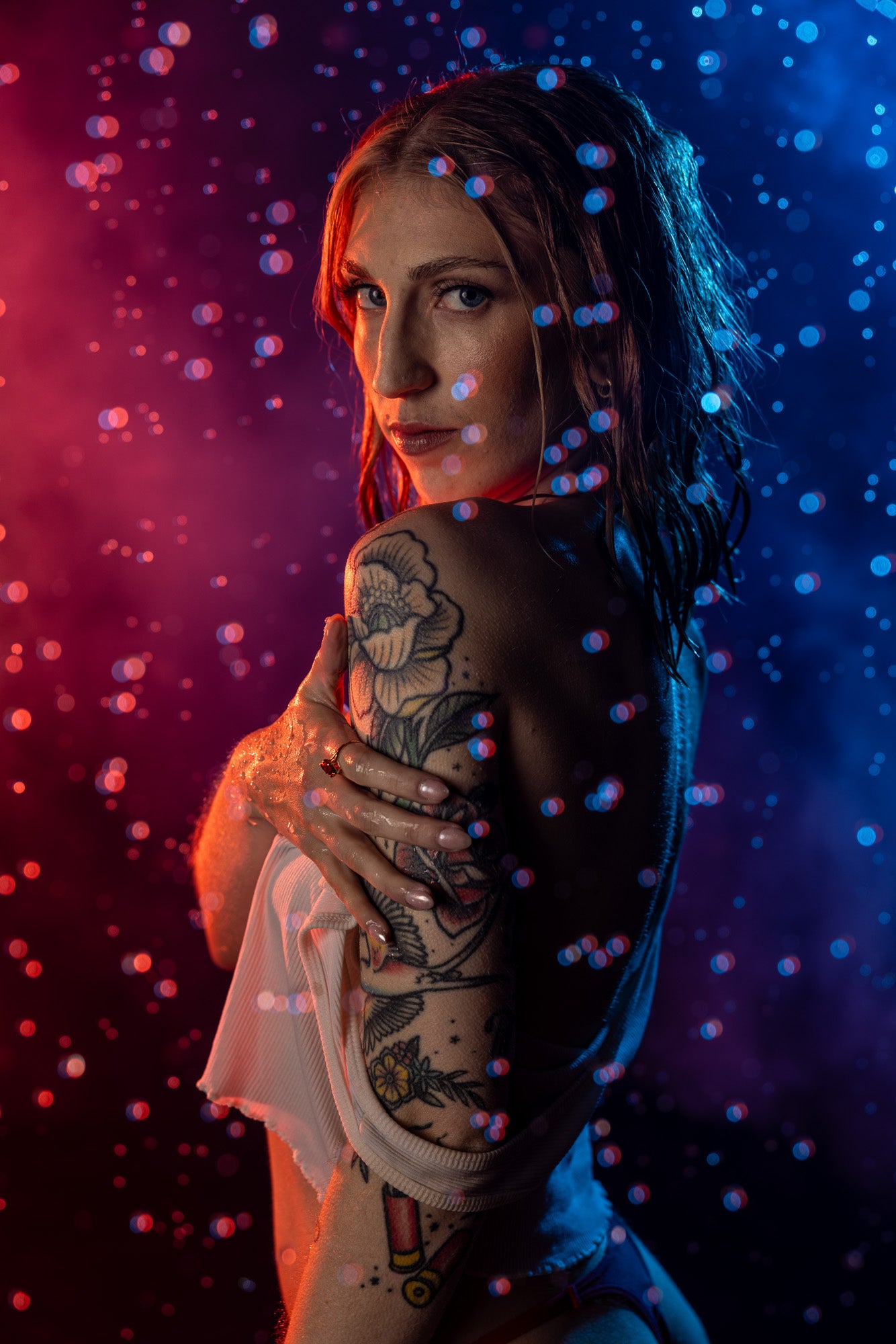 Moody rain-room boudoir portrait featuring intimate posing under dramatic red and blue backlighting, creating a cinematic wet-look atmosphere captured in Wisconsin.