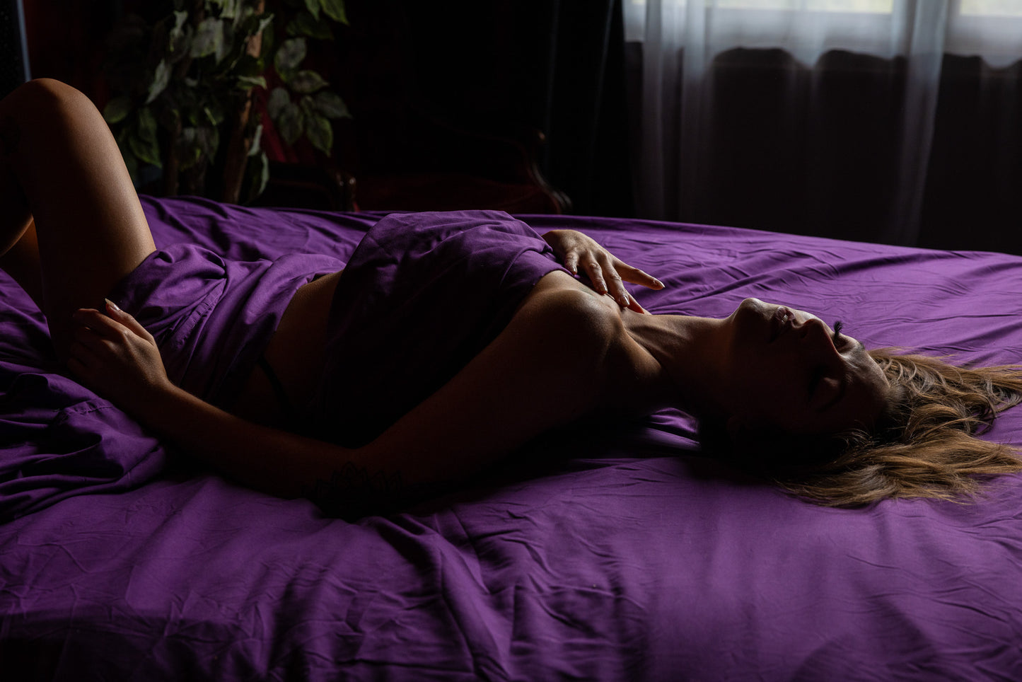 Arching boudoir pose on purple sheets with low, intimate lighting captured in Neenah, Wisconsin at Studio SJ.
