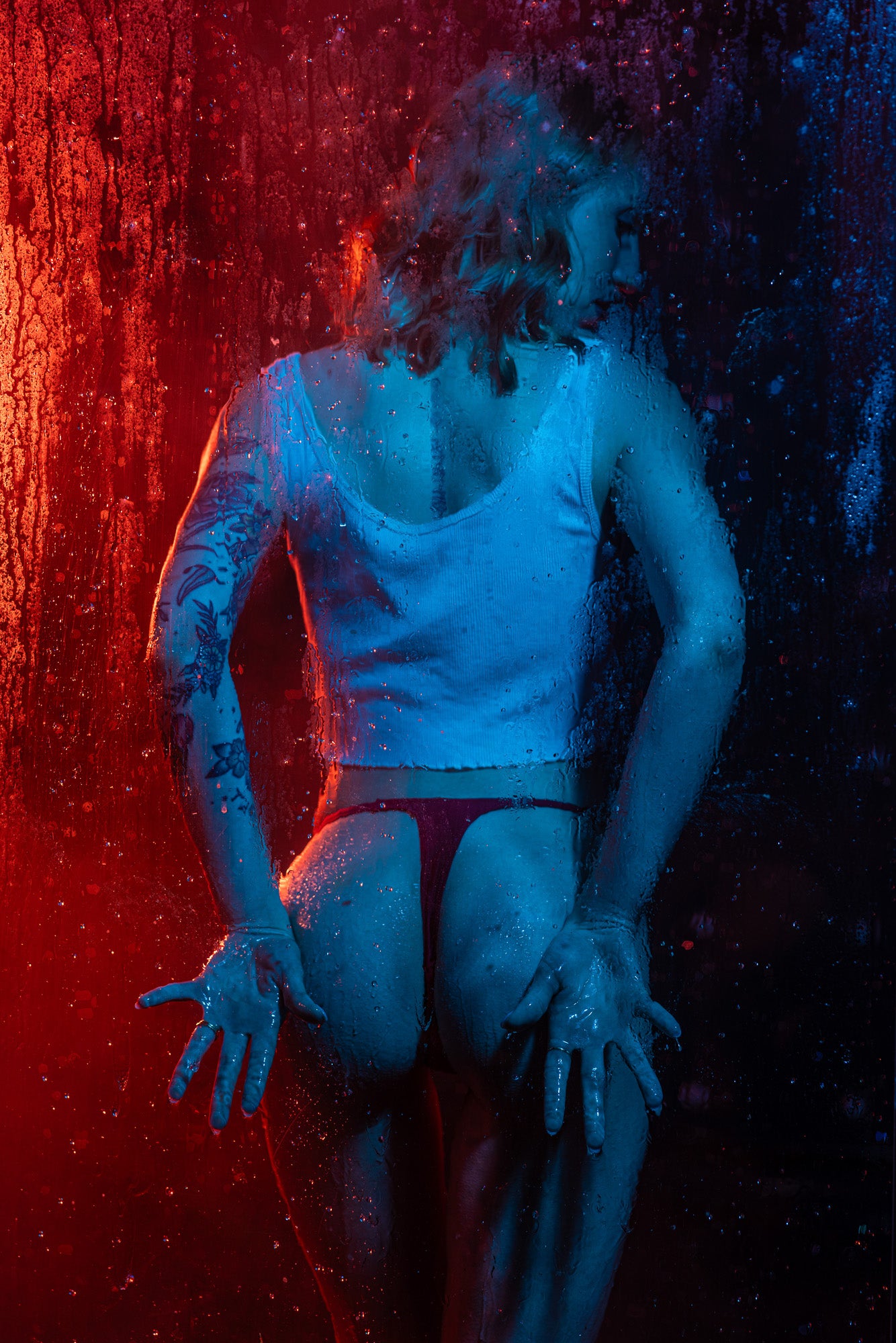 Artistic boudoir silhouette behind a steamy shower glass panel with dramatic red and blue backlighting, creating a moody and modern cinematic look in Wisconsin.