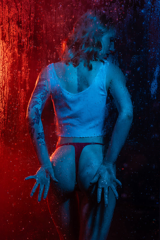 Artistic boudoir silhouette behind a steamy shower glass panel with dramatic red and blue backlighting, creating a moody and modern cinematic look in Wisconsin.