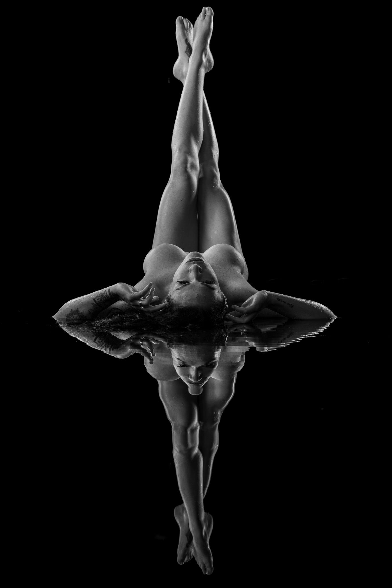 Black-and-white boudoir photo featuring a legs-up pose and water reflection.