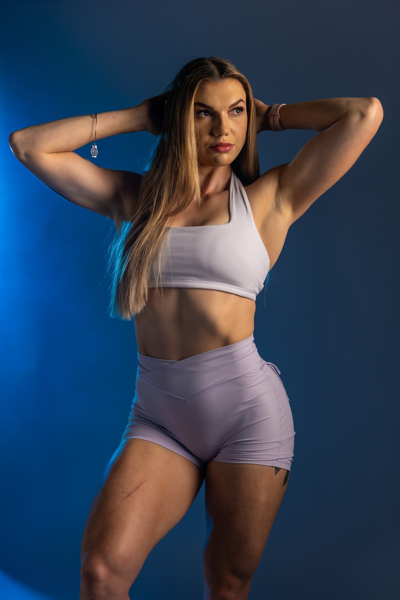 Fitness-glam portrait featuring a woman posed against a blue studio backdrop with dramatic lighting, captured in Appleton, Wisconsin to highlight strength, curves, and a bold athletic aesthetic.