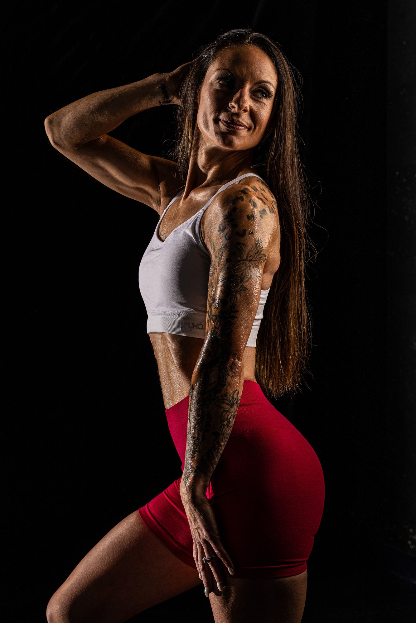 Fitness-glam portrait featuring dramatic water-inspired lighting highlighting muscle tone and curves, creating a bold, athletic boudoir aesthetic.